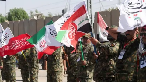 Reuters Iranian military personnel stand in a line waving red, white, green and black flags.