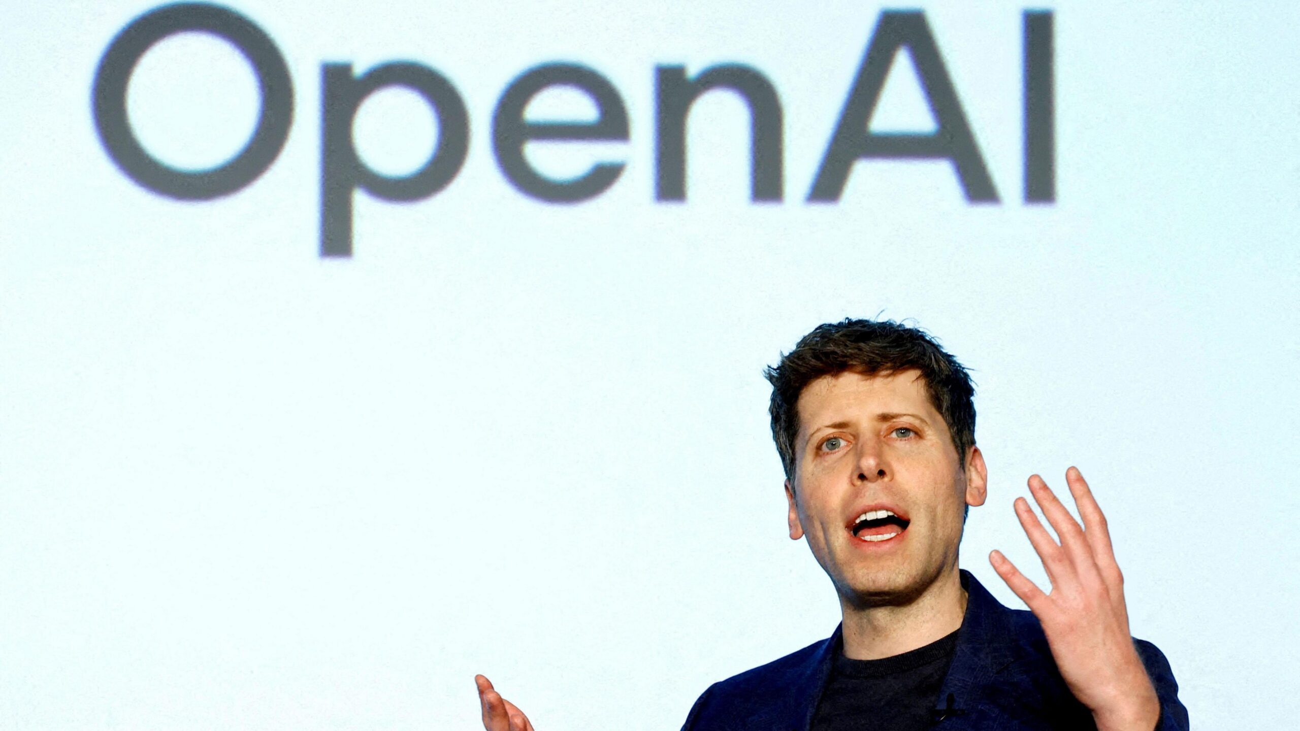 OpenAI CEO Sam Altman speaking on a stage gesturing with his hands.