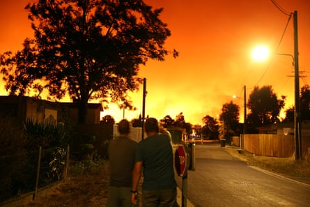 People point to the orange sky lit by fires in a residential street in Le Porge