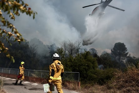 A helicopter drops water over a burning area