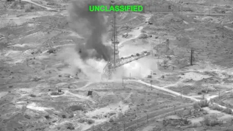 Reuters Smoke rises from an explosion at an unknown location, during what U.S. Central Command (CENTCOM) says are strikes on Iran. The image is black and white and there is green text at the top saying 'unclassified'